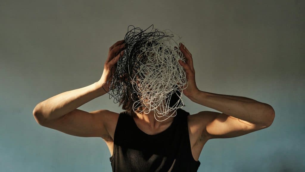A person holding their head with a chaotic scribble of wire or lines obscuring their face, representing anxiety.