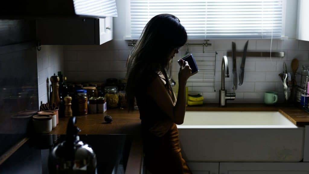 A woman having coffee while standing near the sink in the kitchen.