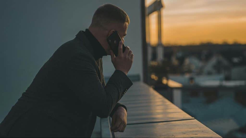 A man leaning on a balcony and talking on his phone at sunset.