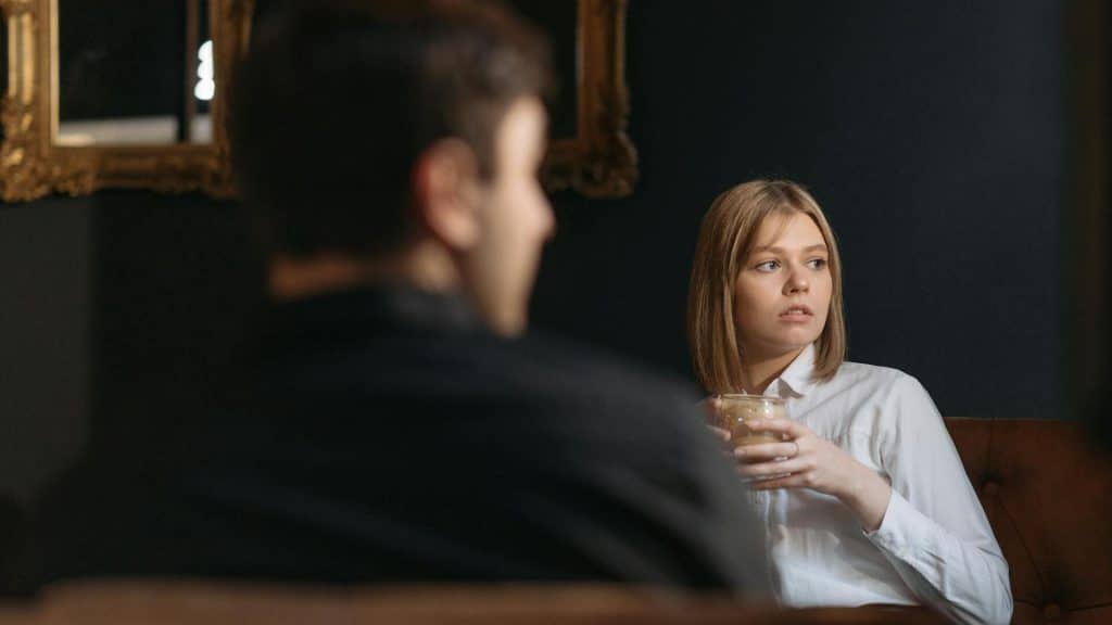 A woman holding a drink, sitting across from a man.