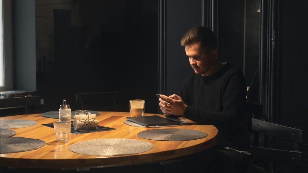 A man sitting at a dining table while looking at his phone.