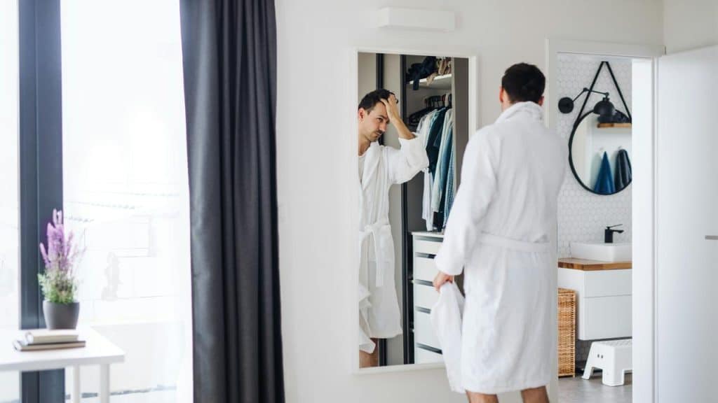 A man in a robe looking at himself in a mirror.