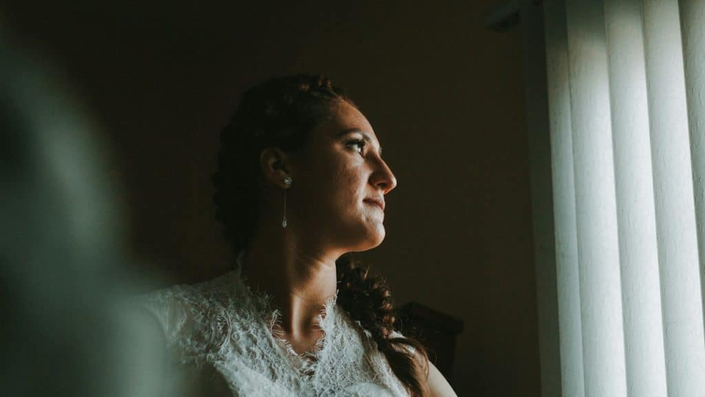 A woman looking out of a window across which blinds are drawn.