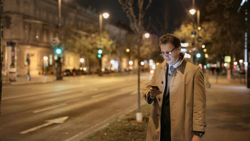 A person stands on a city street at night checking a smartphone.