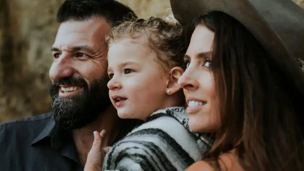 A close-up of two adults and a young child smiling together outdoors.