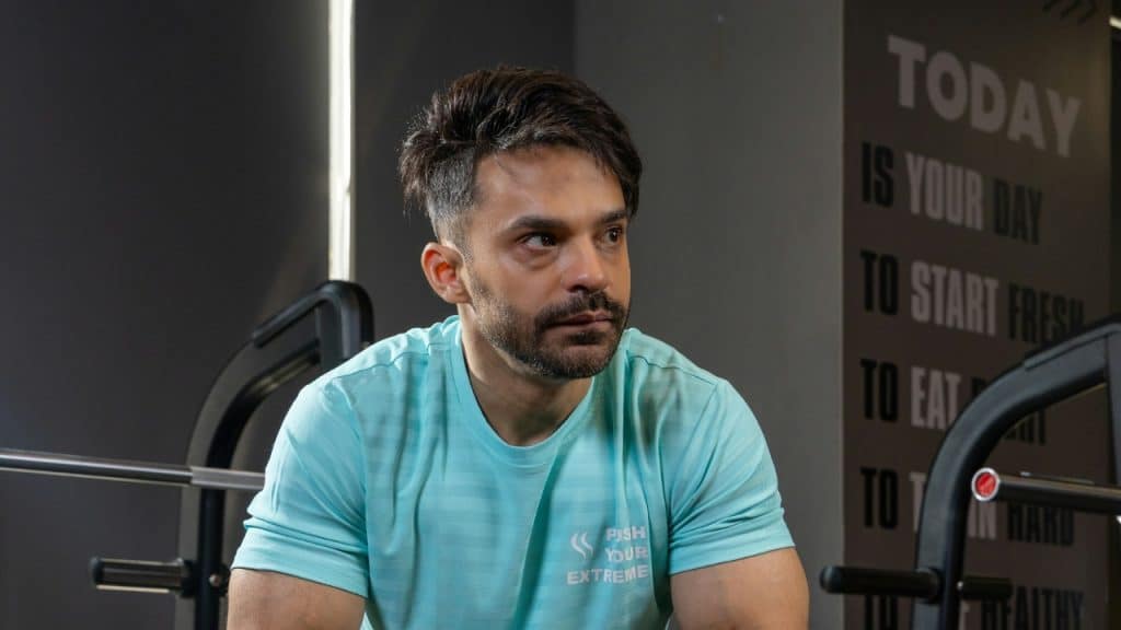 A man in a light blue athletic shirt sits in a gym looking to the side.