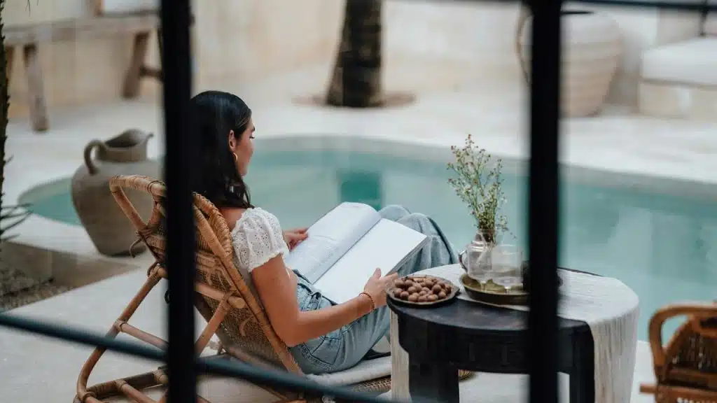 A woman relaxing by a pool while reading a book.