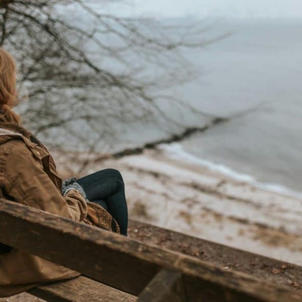 A person sitting on a wooden bench overlooking a quiet beach and calm sea.