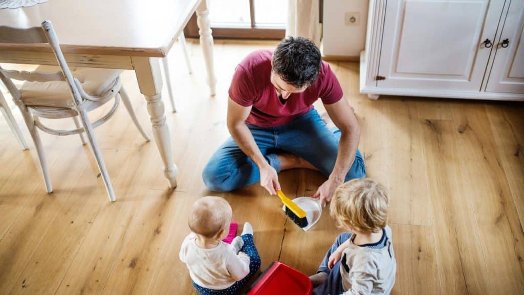 A man sweeping the floor as two young children sit nearby.