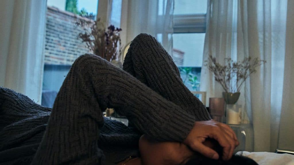 A person resting indoors with an arm over their face near a softly lit window.