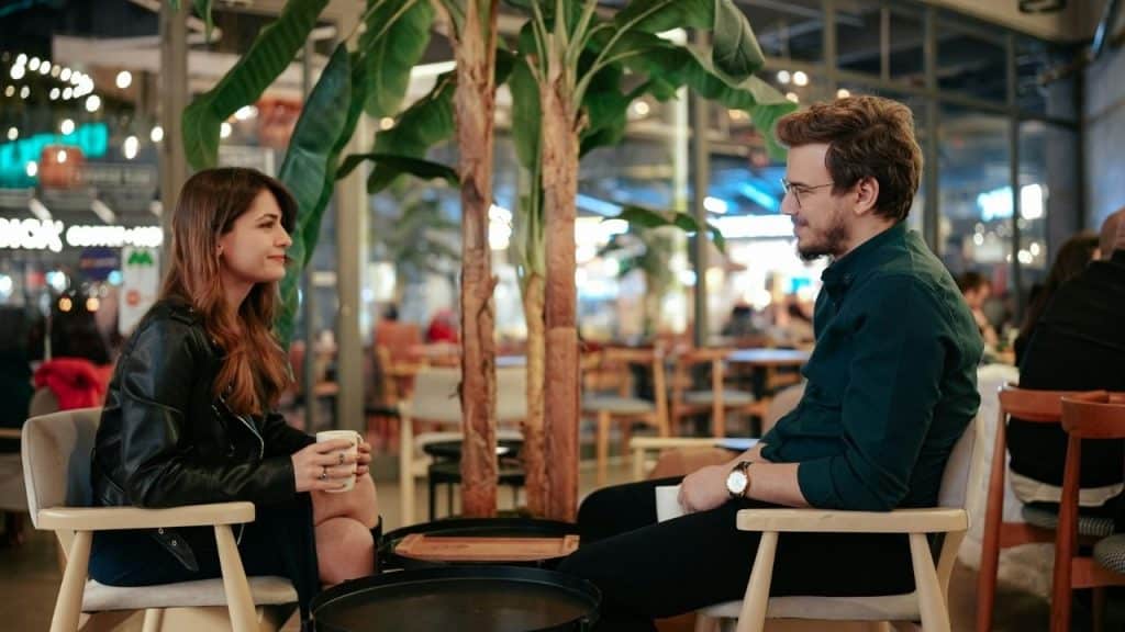 A man in a green shirt sits across from a woman in a leather jacket.