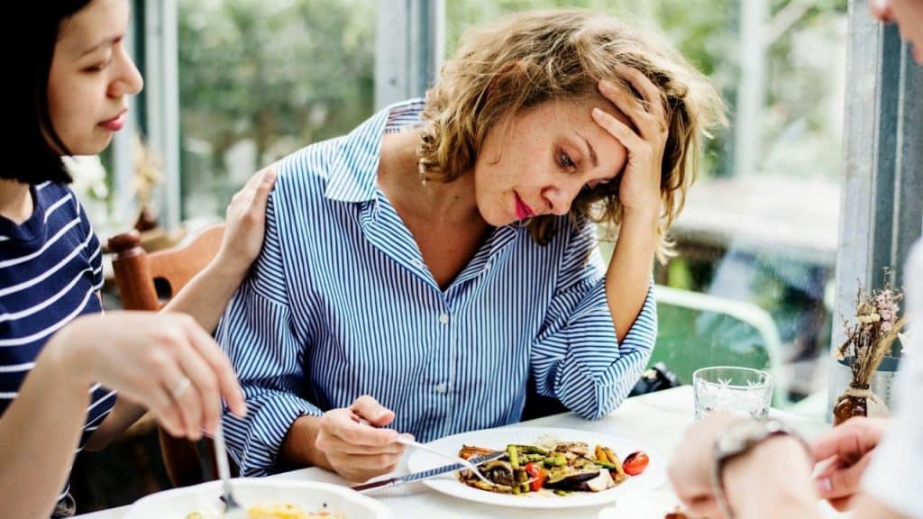 A woman in a striped shirt rests her head in her hand at a table.
