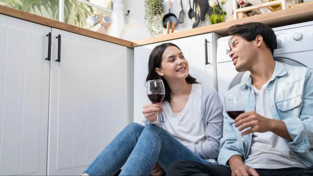 A man and woman sitting on the floor with wine on their hand