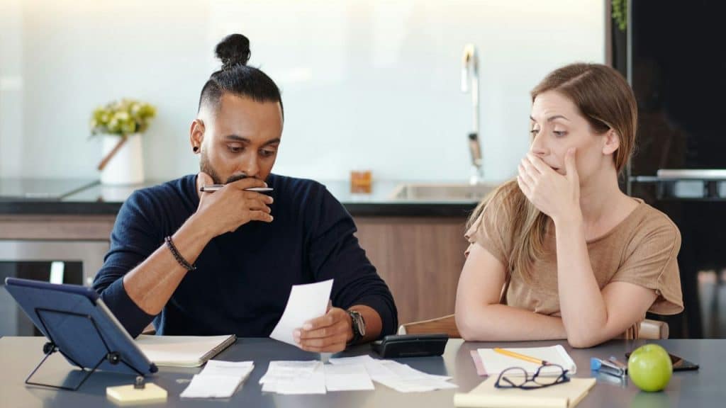 A man and woman sit at a table looking at papers, calculators, and a tablet.