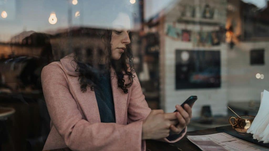 A woman checking her phone while sitting at a café table by a window.