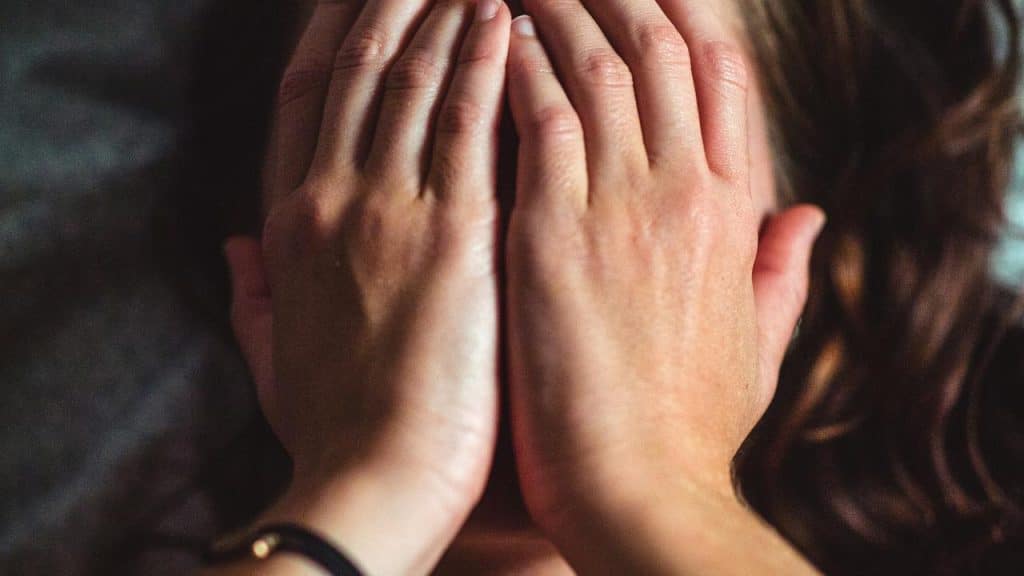 A person covering their face with both hands in a close-up view.