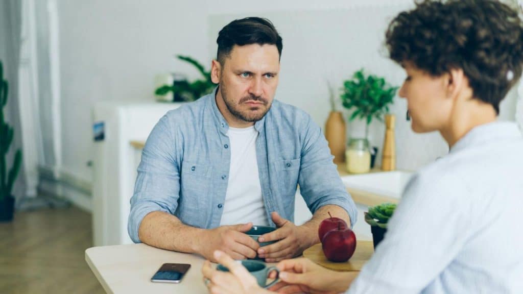 A man with a serious expression sits at a table across from a woman.