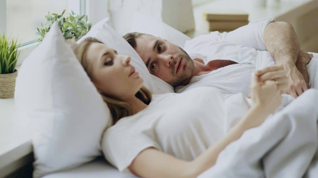 A man holding the hands of his wife, who is being upset while they are lying next to each other on the bed.