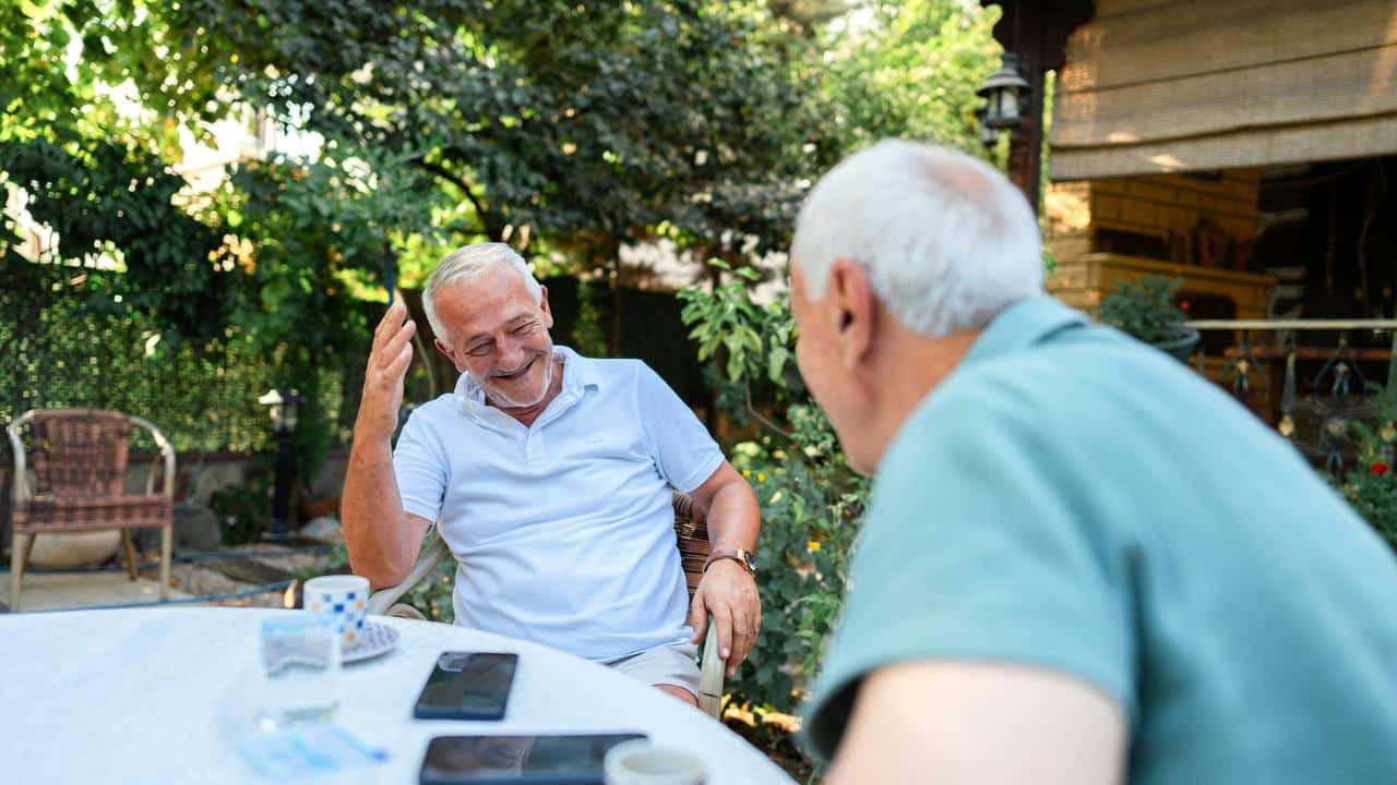 A pair of senior men smiling and having a happy conversation outdoors.