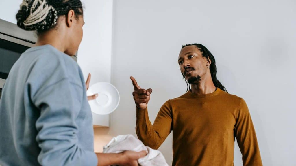 A man with dreadlocks points his finger while speaking to a woman holding a saucer.