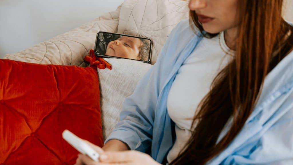 A woman holds a phone near a pillow featuring a picture of a sleeping baby.