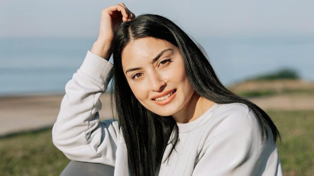 A woman smiling and looking at the camera while sitting outdoors.