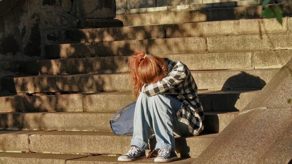 A person sitting on stone steps with head resting on their knees.