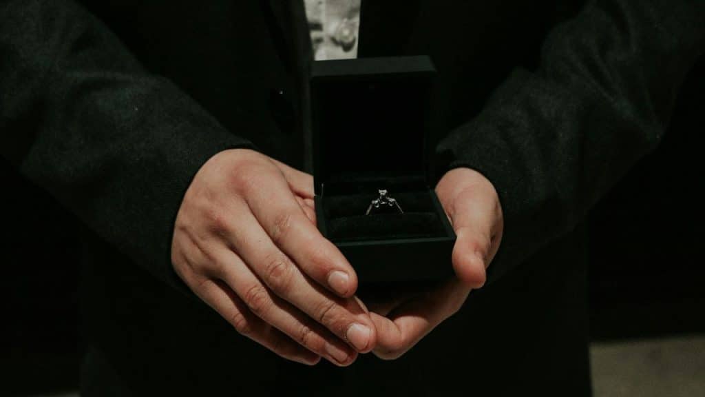 Close-up of a person in a dark suit holding an open black ring box.