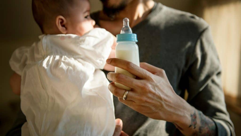 A caregiver holding a baby while offering a bottle of milk.