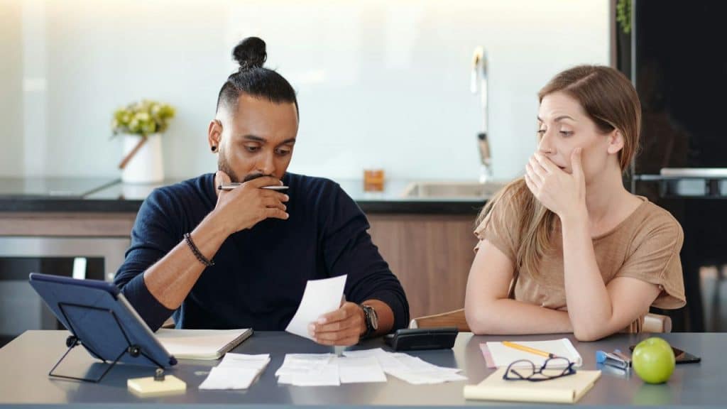 A man with a hair bun reviews paper receipts while a woman watches with concern.