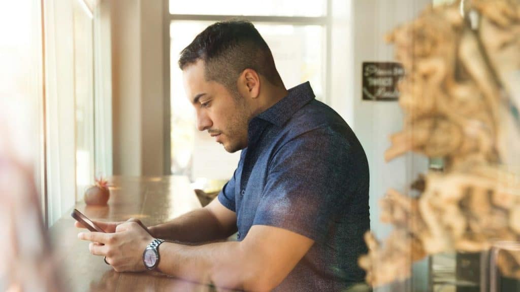 A man sits at a bar, looking down at his phone.