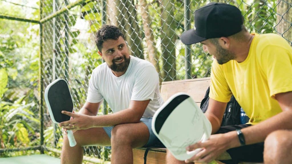 A photo of two men with pickleball paddles talking on a bench.