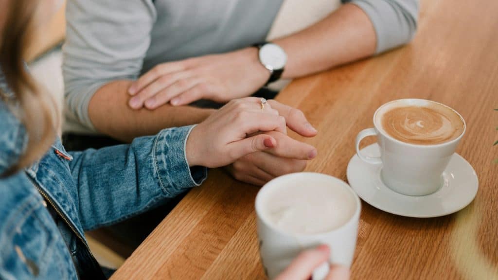 A couple holding hands while having coffee at a table.