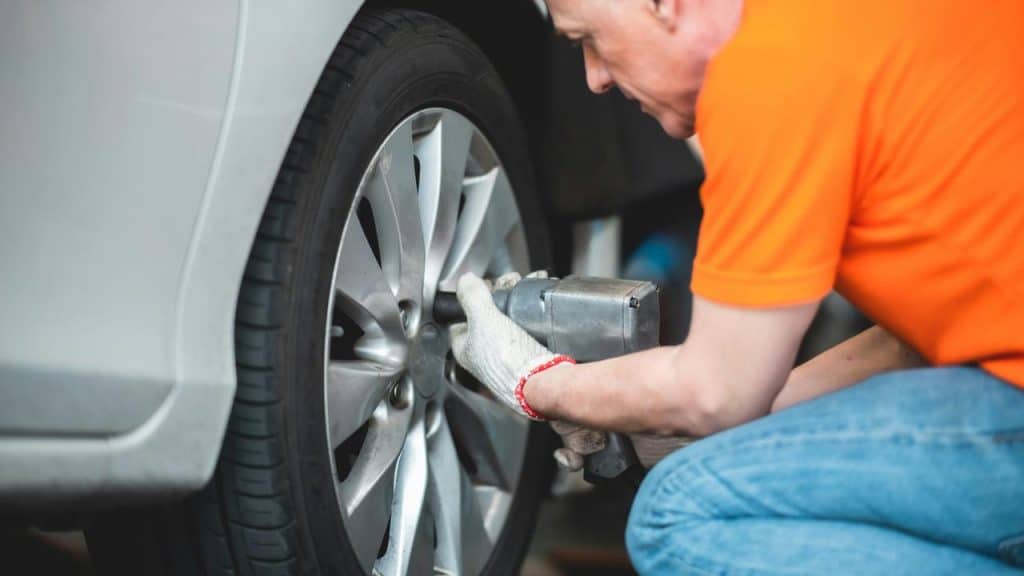 A mechanic in an orange shirt working on a car wheel.