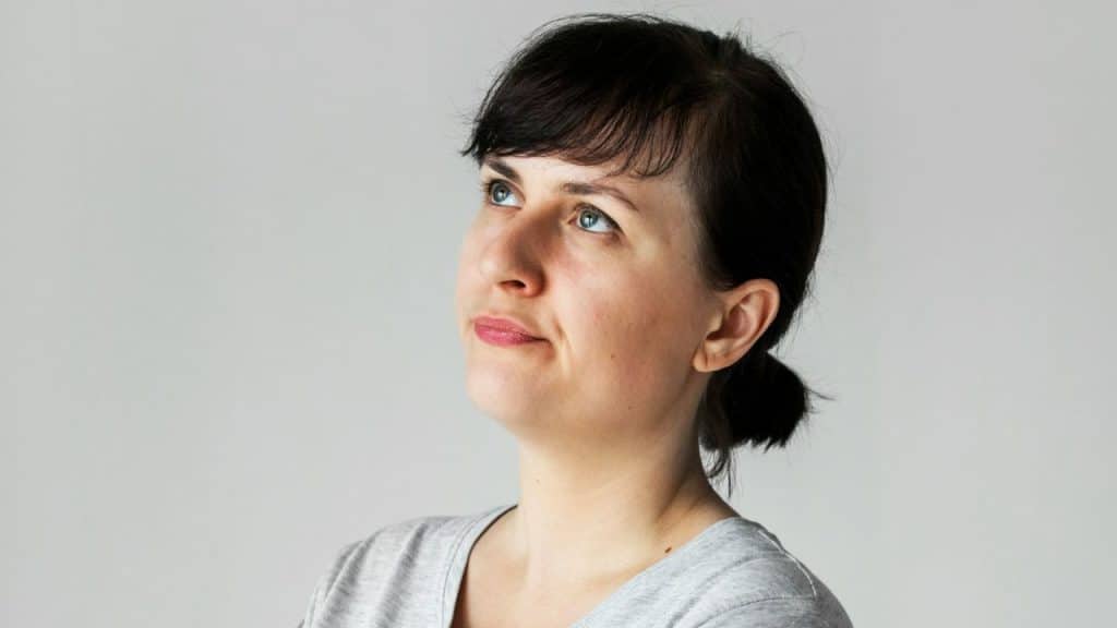 A woman with dark hair and bangs looks upward with a neutral expression.