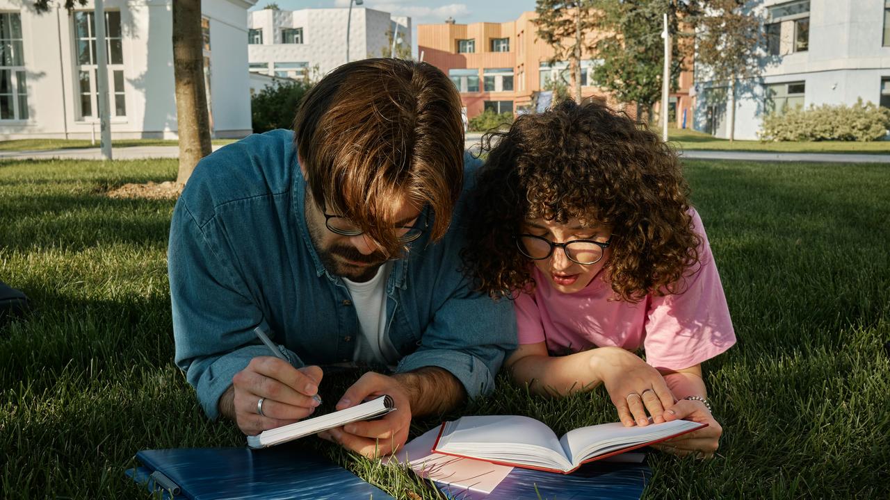 A couple studying together on the grass with notebooks.