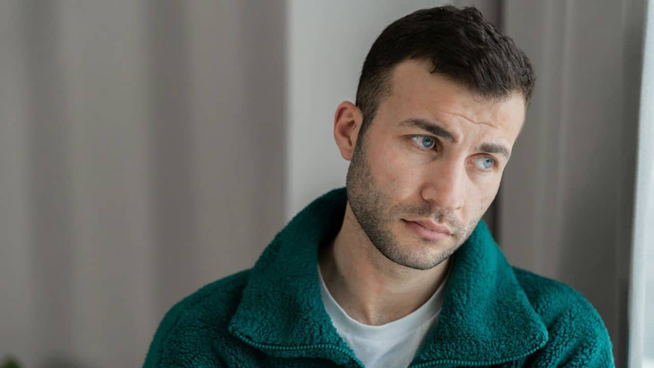 A man with blue eyes and a beard looks off-camera while wearing a teal fleece jacket.