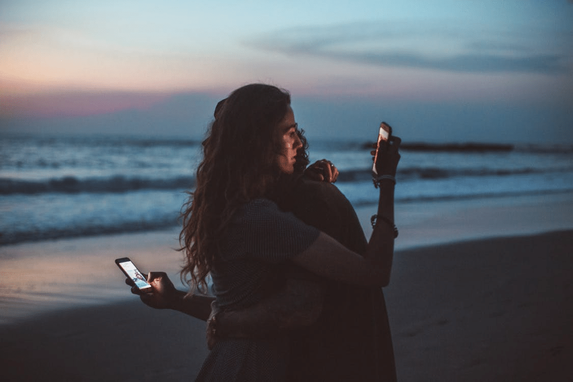 A couple using their phone while hugging
