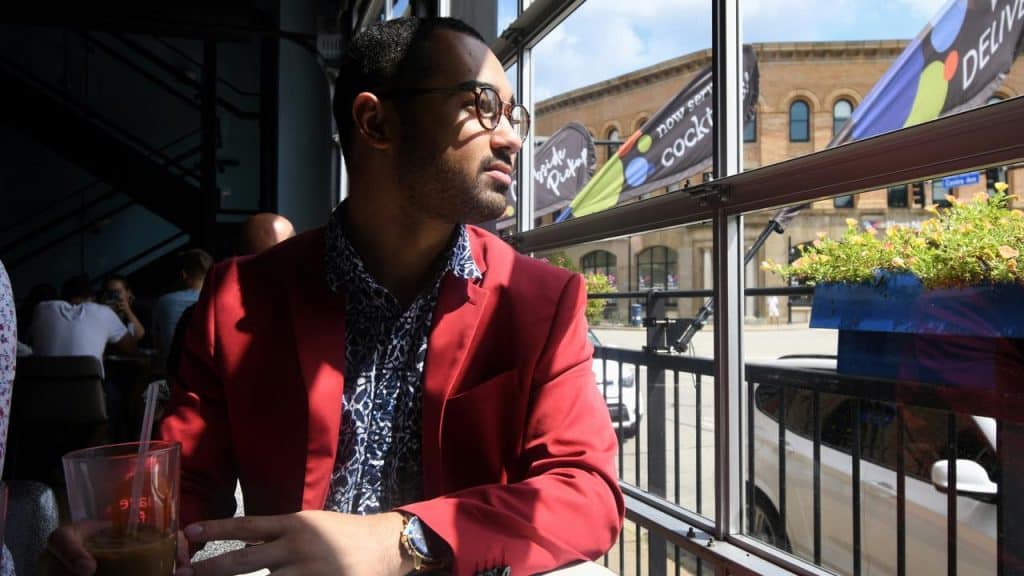 A man in a red blazer holding a drink and gazing out a café window.