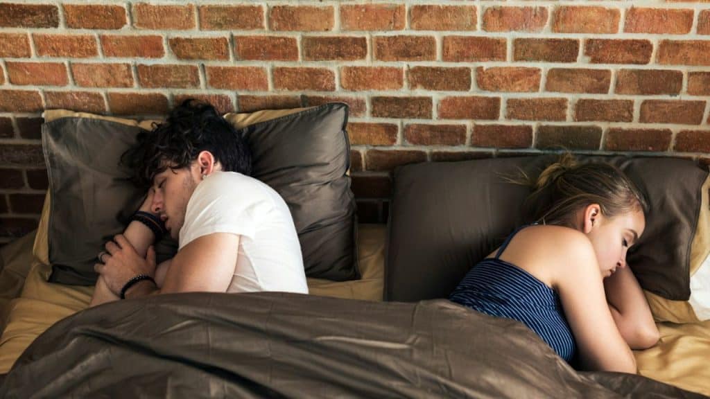 A man and a woman sleep in separate beds, both facing away from each other.