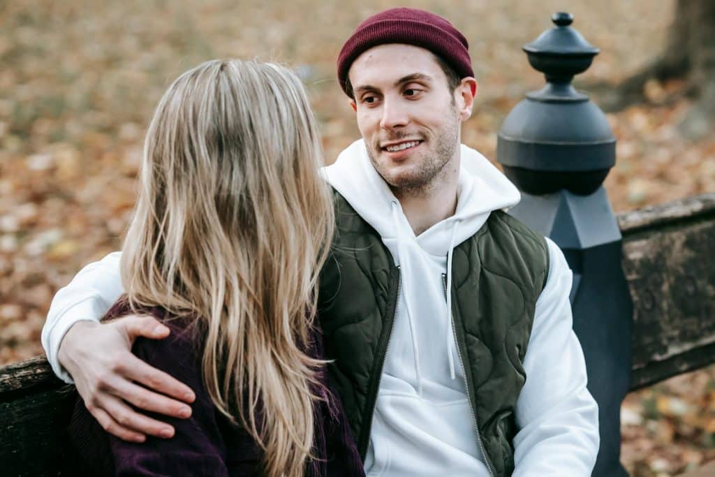 The man is looking lovingly at his woman while sitting on a park bench.