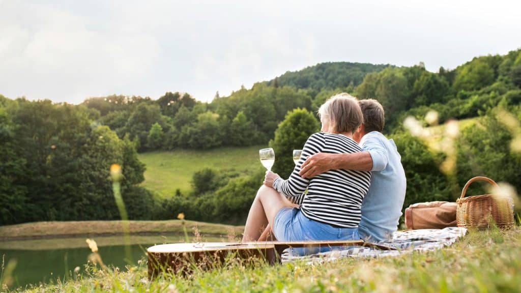 A couple sitting on a blanket and enjoying wine while overlooking a green countryside.