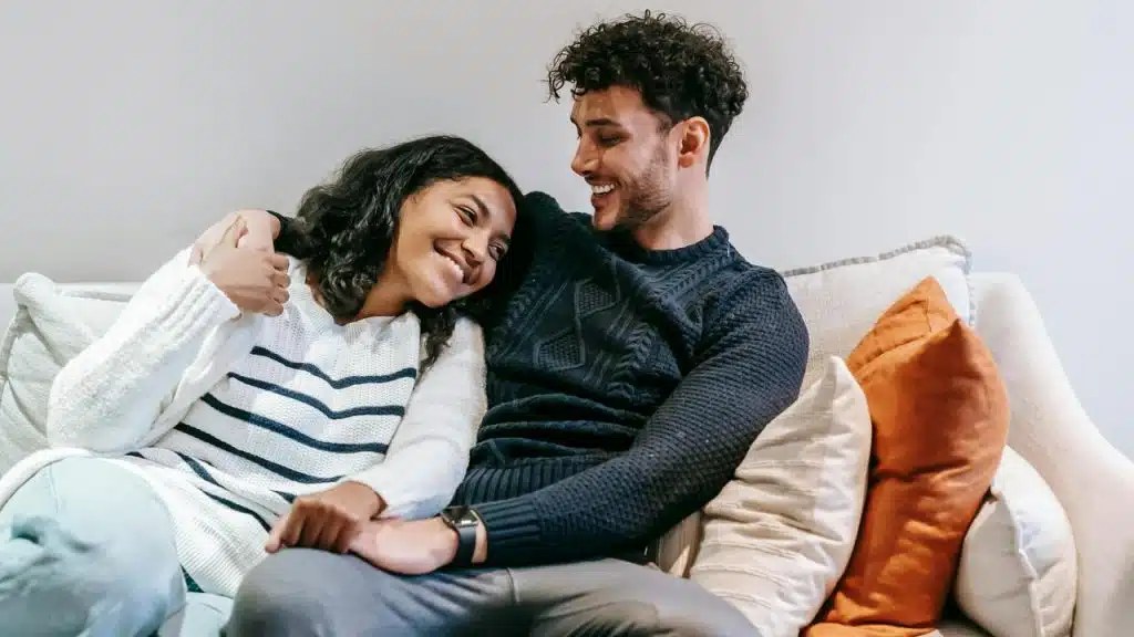 A smiling couple sitting close together on a couch with their arms around each other.