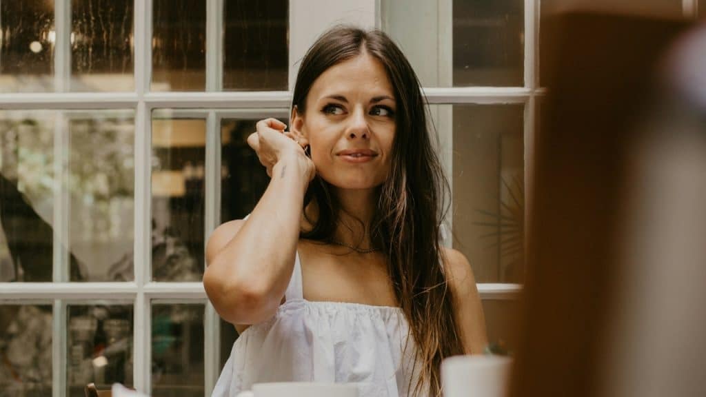 A woman with long dark hair sits by a window and looks off to the side.