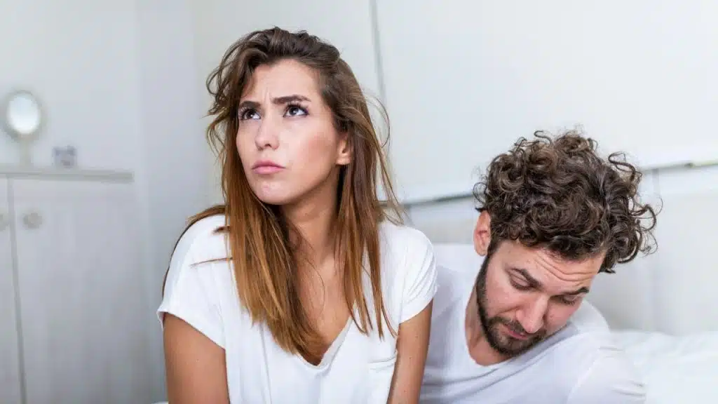 A woman looks upward with a frustrated expression while a man sits slumped behind her.