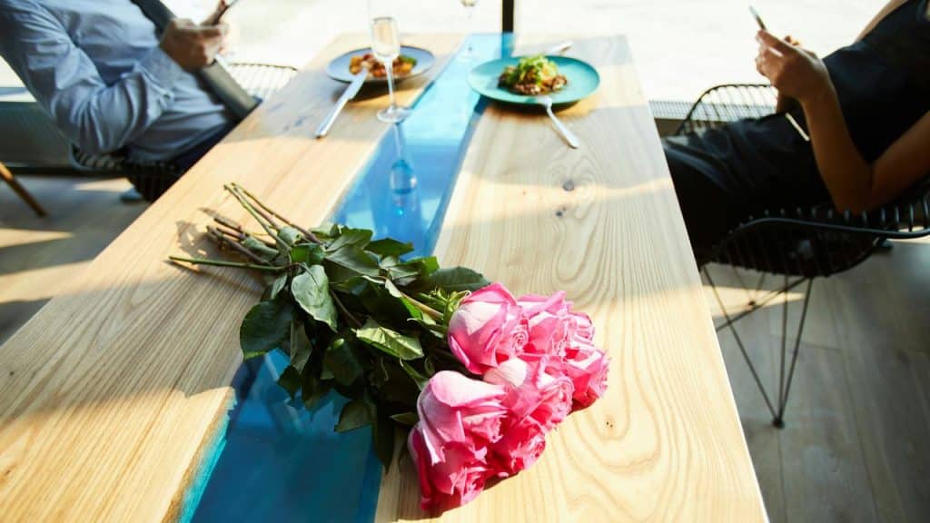 A bouquet of pink roses on a restaurant table as two people look at their phones.