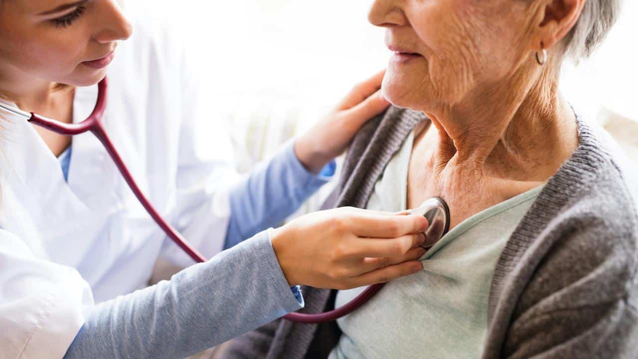 A healthcare worker using a stethoscope on an older woman.