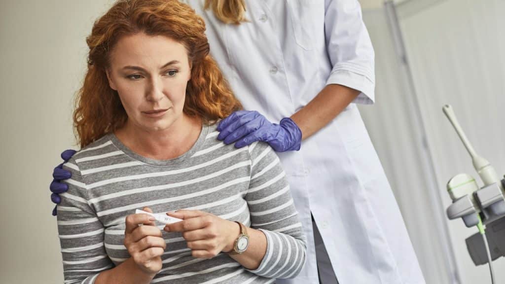 A woman is checking a pregnancy strip and feeling disappointed while her caring doctor is holding her shoulders.