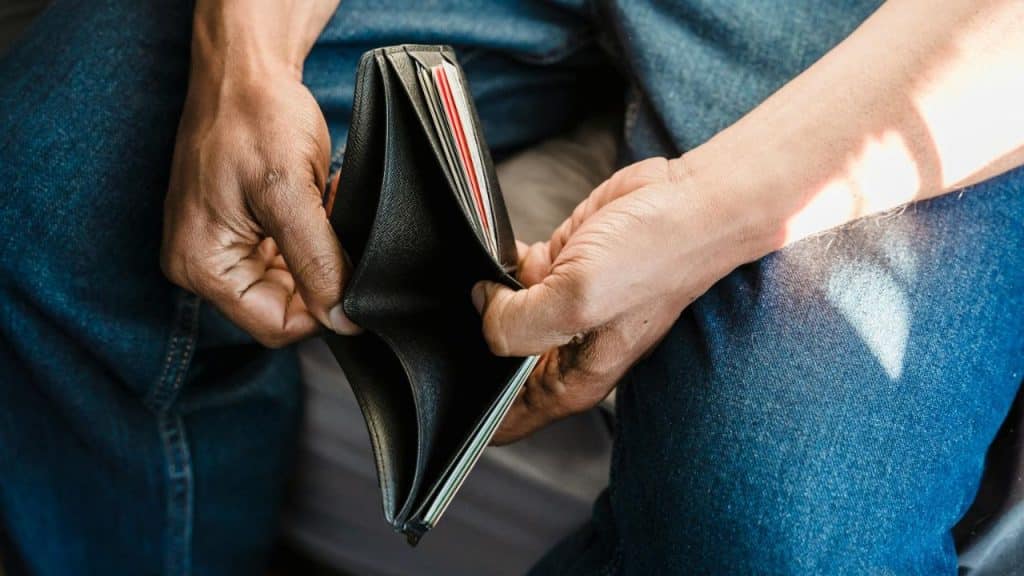 A close-up view of two hands holding open an empty black leather wallet over denim.