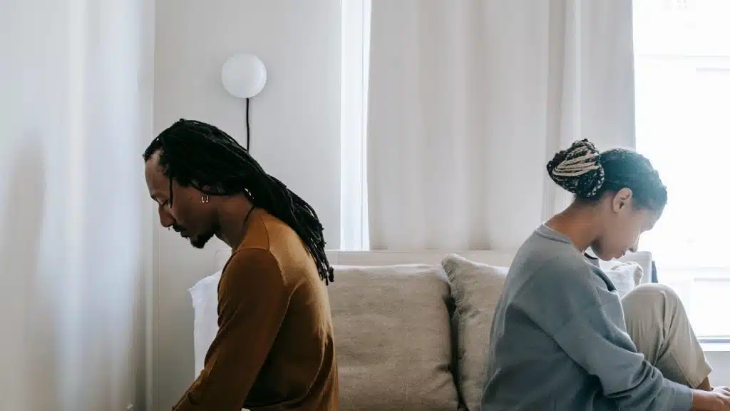 A couple not talking to each other and sitting with their backs to each other on a bed.